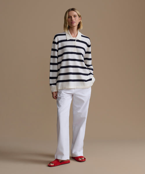 Woman wearing a navy stripe post pullover with white pants on a beige background