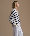Woman wearing a striped Post Pullover and white pants against a beige background