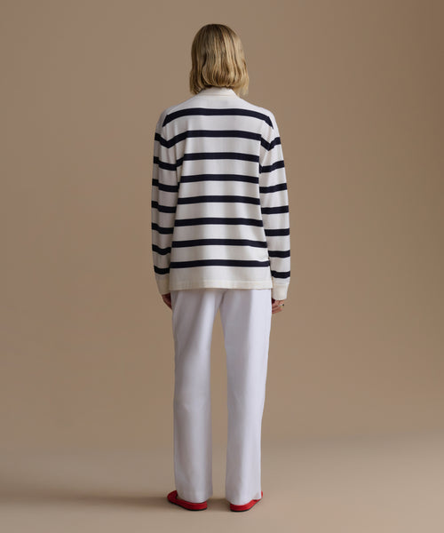 Person wearing a navy stripe Post Pullover and white pants against a beige background
