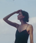 Thumbnail for video: Woman in a black dress standing by the ocean with a soft sky background