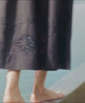 Thumbnail for video: Woman wearing a cream top and navy skirt standing on a rooftop with a scenic view of mountains and sea.