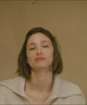 Thumbnail for video: Woman wearing a beige knit cardigan standing among stacked bags against a beige wall.