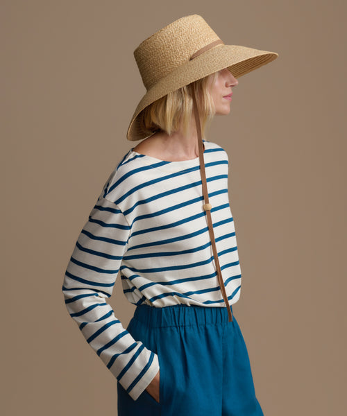 Woman wearing a striped shirt and wide-brimmed hat against a brown background