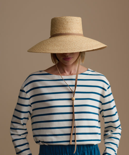 Person wearing a woven hat and a striped shirt against a plain background