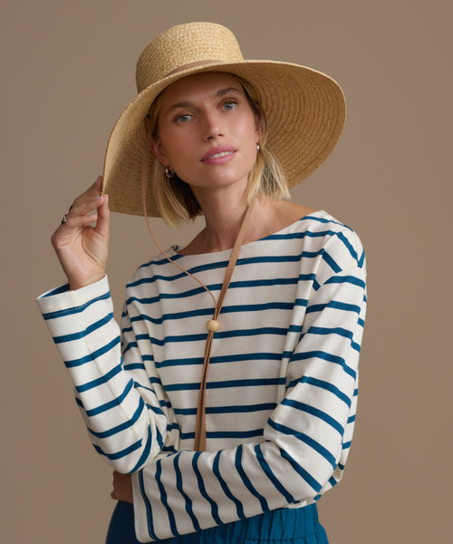 Woman wearing a woven hat and a striped shirt against a beige background