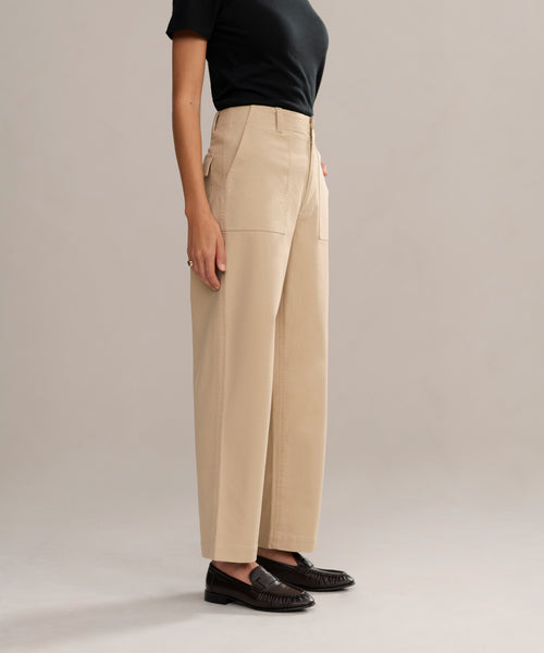 A person is shown from the shoulders down wearing a fitted black short-sleeve top, Ranger Trouser in classic high-waisted beige lightweight twill, and black loafers against a plain light background.
