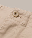 Close-up of the Ranger Trouser’s beige lightweight twill waistband featuring a stitched seam and a tan button above a vertical seam, set against a plain light background.