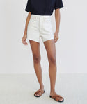 A person stands against a plain light background, wearing a navy short-sleeve shirt, the Low Slung Short in vintage white, and brown slide sandals. Their face is not visible.
