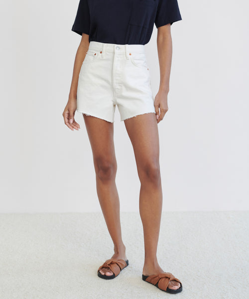A person stands against a plain light background, wearing a navy short-sleeve shirt, the Low Slung Short in vintage white, and brown slide sandals. Their face is not visible.