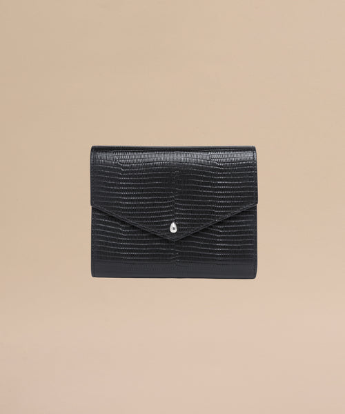 The Reece Leather Wallet, a black textured clutch with a flap closure and silver teardrop accent, is shown on a plain beige background—ideal as a mid-size wallet.