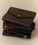 A trio of Reece Leather Wallets in brown and black, each with unique textures like embossed leather and zipper closures, displayed on a light beige surface.
