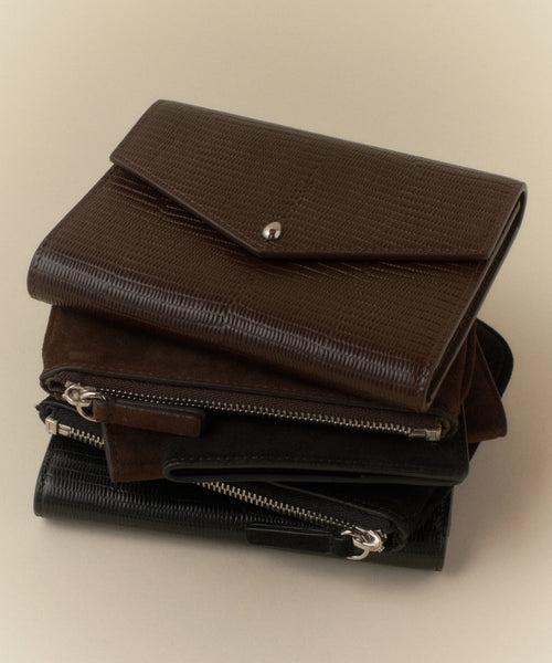 A trio of Reece Leather Wallets in brown and black, each with unique textures like embossed leather and zipper closures, displayed on a light beige surface.