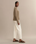 A woman stands sideways, facing the camera, wearing the Ren jean in a wide-leg silhouette with a tan sweater and brown sandals, set against a plain beige background.