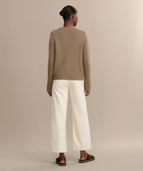 A person stands facing away in a brown sweater, brown sandals, and the Ren jean—off-white, wide-leg jeans made from regenerative cotton—against a plain beige background.