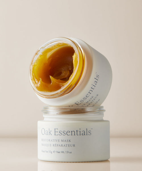 An open jar of Restorative Mask with the lid placed upside down on top showcases the thick, golden-yellow formula enriched with Avocado Oil inside, while the product label remains visible on the jar.
