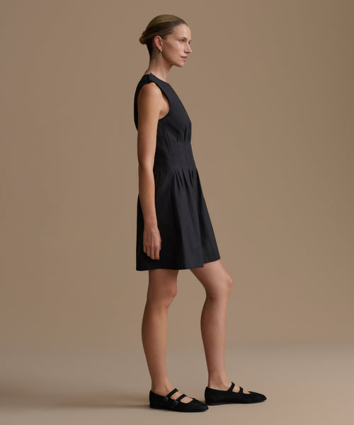 Woman wearing a black sleeveless dress against a beige background