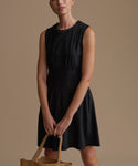 Woman wearing a black sleeveless dress holding a woven bag against a brown background