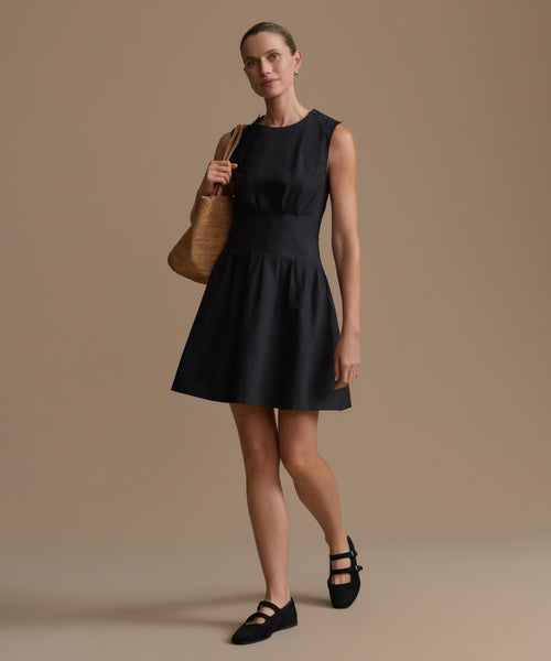 Woman wearing a black dress holding a brown woven bag against a beige background