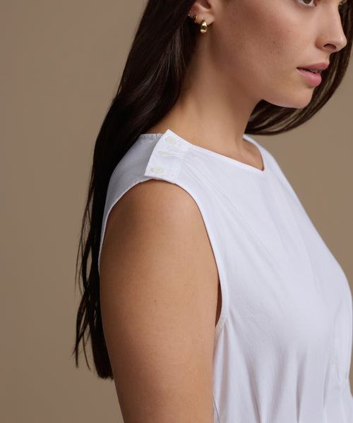 Woman wearing a white sleeveless top against a beige background