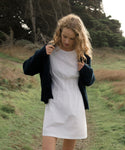 Woman in a white dress and navy blue cardigan standing in a grassy field.