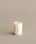 A cream-colored Mini Topanga Glass Candle, hand-poured in Los Angeles with a natural wax blend, sits in a jenni kayne-labeled glass container. The label lists its scents: green leaves, eucalyptus, and grapefruit on a beige surface.