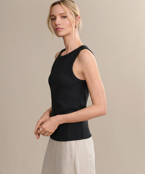 A woman with blonde hair in a low bun wears a sleeveless black Cotton Rib Tank and light beige pants, posing in profile against a plain light beige background.