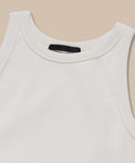 A close-up of the Cotton Rib Tank in white, featuring a rounded neckline and heavy rib fabric, laid flat on a beige background—ideal for layering.