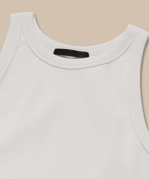A close-up of the Cotton Rib Tank in white, featuring a rounded neckline and heavy rib fabric, laid flat on a beige background—ideal for layering.