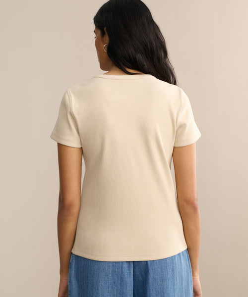A woman with long dark hair is seen from behind wearing a fitted, short-sleeved Rib Tee and blue jeans, standing against a plain, neutral background.