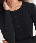 A person with curly hair wears the Ribbed Finley Cardigan—an elegant, fitted black cardigan with 90s-inspired ribbing and front black buttons. Their hand near their neck partially hides their face.