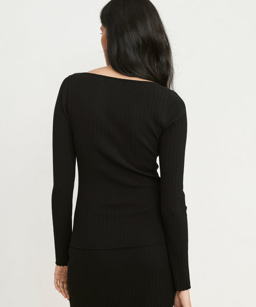 A woman with long dark hair is shown from the back, wearing a fitted Ribbed Long-Sleeve scoop-neck top and a matching ribbed skirt against a plain light-colored background.