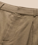 Close-up of the Riley Trouser’s waistband and upper section, highlighting belt loops, a pleat, and part of a front pocket against a beige background. Crafted from lightweight linen for summer comfort.