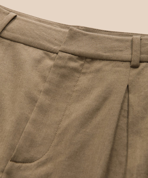 Close-up of the Riley Trouser’s waistband and upper section, highlighting belt loops, a pleat, and part of a front pocket against a beige background. Crafted from lightweight linen for summer comfort.