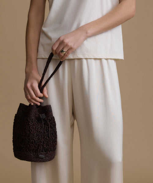 Model holding a brown raffia bucket bag against a beige background.