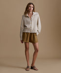 Woman wearing a beige cardigan and brown shorts against a beige background