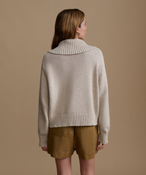 Woman wearing a beige sweater and brown shorts against a beige background