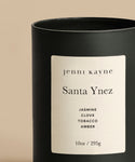 A black jar with a white label reads “Santa Ynez Glass Candle” and features notes of jasmine, clove, tobacco, and amber. Hand-poured in Los Angeles, this rustic scented candle comes in a 10oz / 295g size.