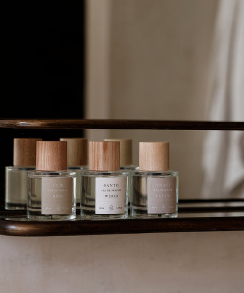 A glass bottle of Santo Wood Eau De Parfum with a wooden cap sits on a metal shelf, its minimalist label highlighting this clean, non-toxic fragrance.