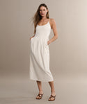 A woman stands against a beige background wearing a sleeveless white midi dress with pockets and the Scarlett Heeled Sandal. Her long, straight hair and relaxed pose add to her confident, summery style.