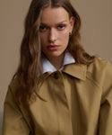 Woman wearing a beige trench coat against a neutral background
