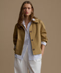 Woman wearing a mustard yellow jacket over a white shirt and beige pants on a brown background