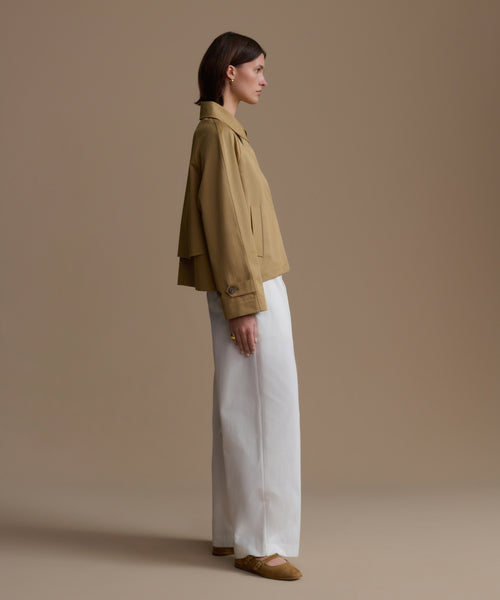 Woman wearing a beige jacket and white pants against a beige background