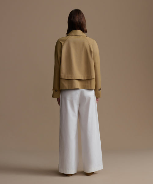 Person wearing a beige jacket and white pants on a brown background