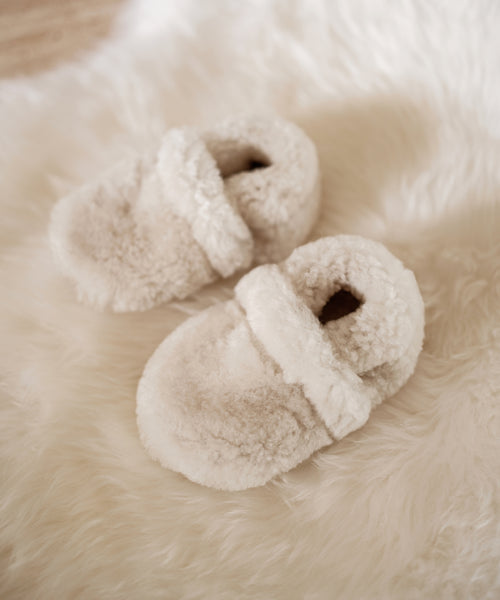 Shearling Baby Booties in soft ivory rest on a matching fuzzy rug, creating a warm and inviting atmosphere for your little one.