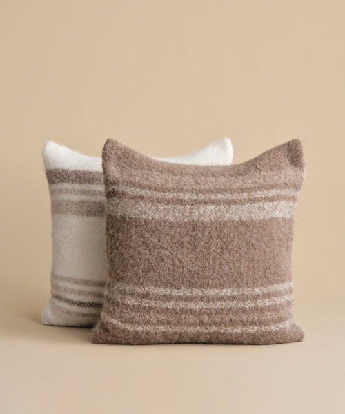 A pair of rectangular Sheridan Pillows with a fuzzy alpaca blend and horizontal stripes: one in brown and beige at the front, the other in off-white and light gray at the back, displayed on a beige background.