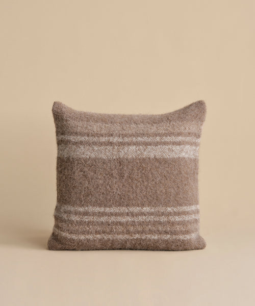 A square brown Sheridan Pillow with white horizontal stripes sits centered on a plain beige background, showcasing its soft, textured look.