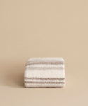 The Sheridan Throw, crafted from a cozy alpaca blend with fluffy beige and gray horizontal stripes, is neatly folded and displayed on a plain light tan background.