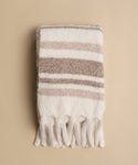 The Sheridan Throw, a soft alpaca blend with beige and white stripes and fringe tassels, is folded and displayed on a neutral beige background.