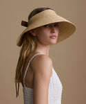 Woman wearing a straw visor hat against a beige background