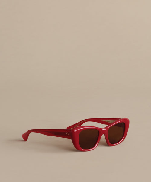 A pair of red, square-framed Sierra Sunglasses with dark lenses offers 100% UV protection, displayed on a plain beige surface against a matching beige background.